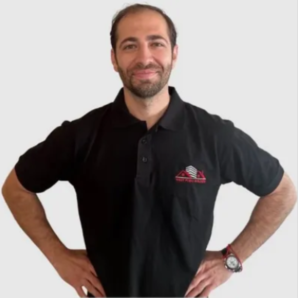 Smiling bearded man in a black collared shirt against a plain light background.