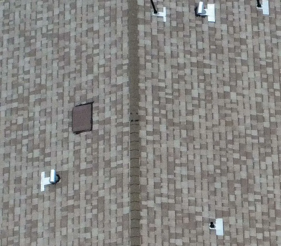 Overhead view of a gray-brown asphalt shingle roof with multiple small roof penetrations and a central ridge