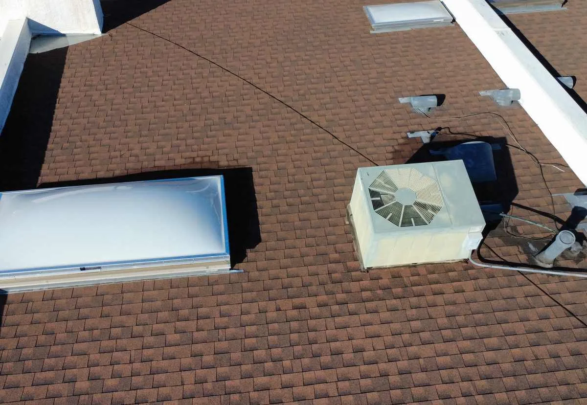 Brown asphalt shingle roof with two skylights, a rooftop HVAC unit, vent pipes and cabling across the surface