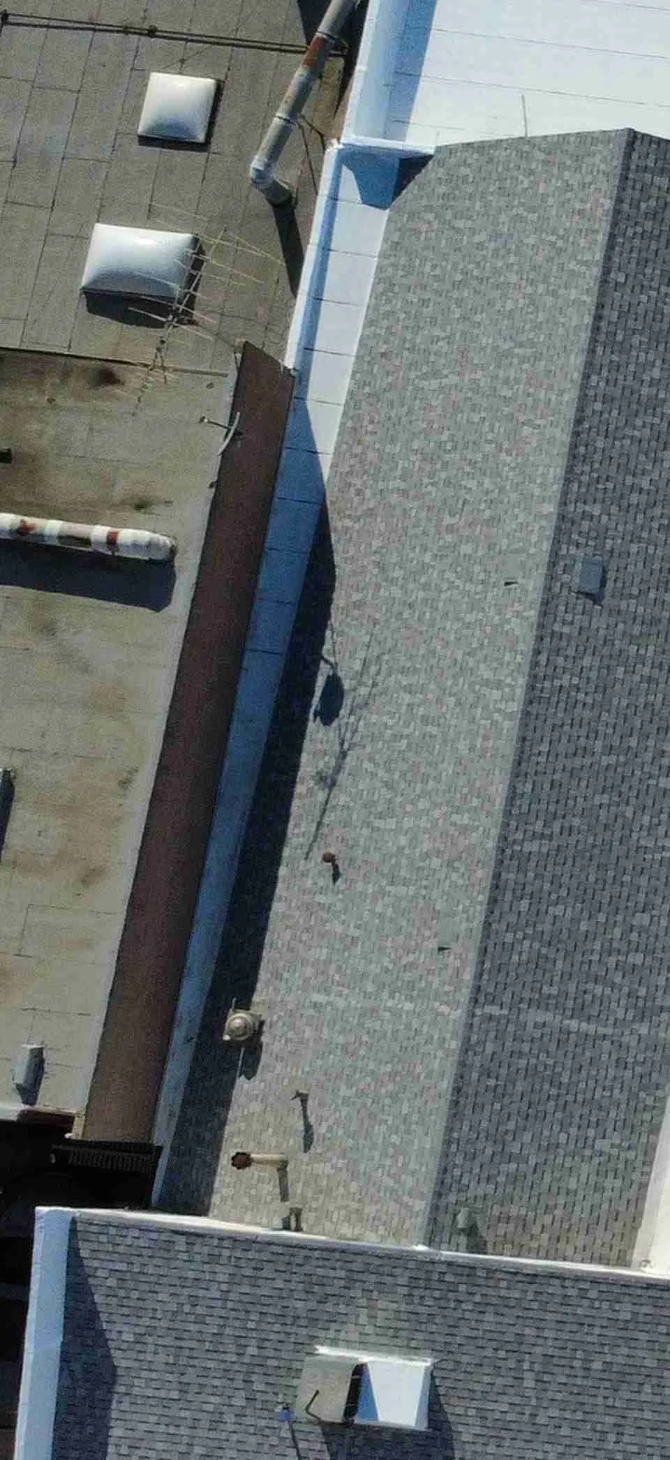 White low-slope roof sections meeting gray shingle areas, with rooftop equipment and solar panels on nearby roofs
