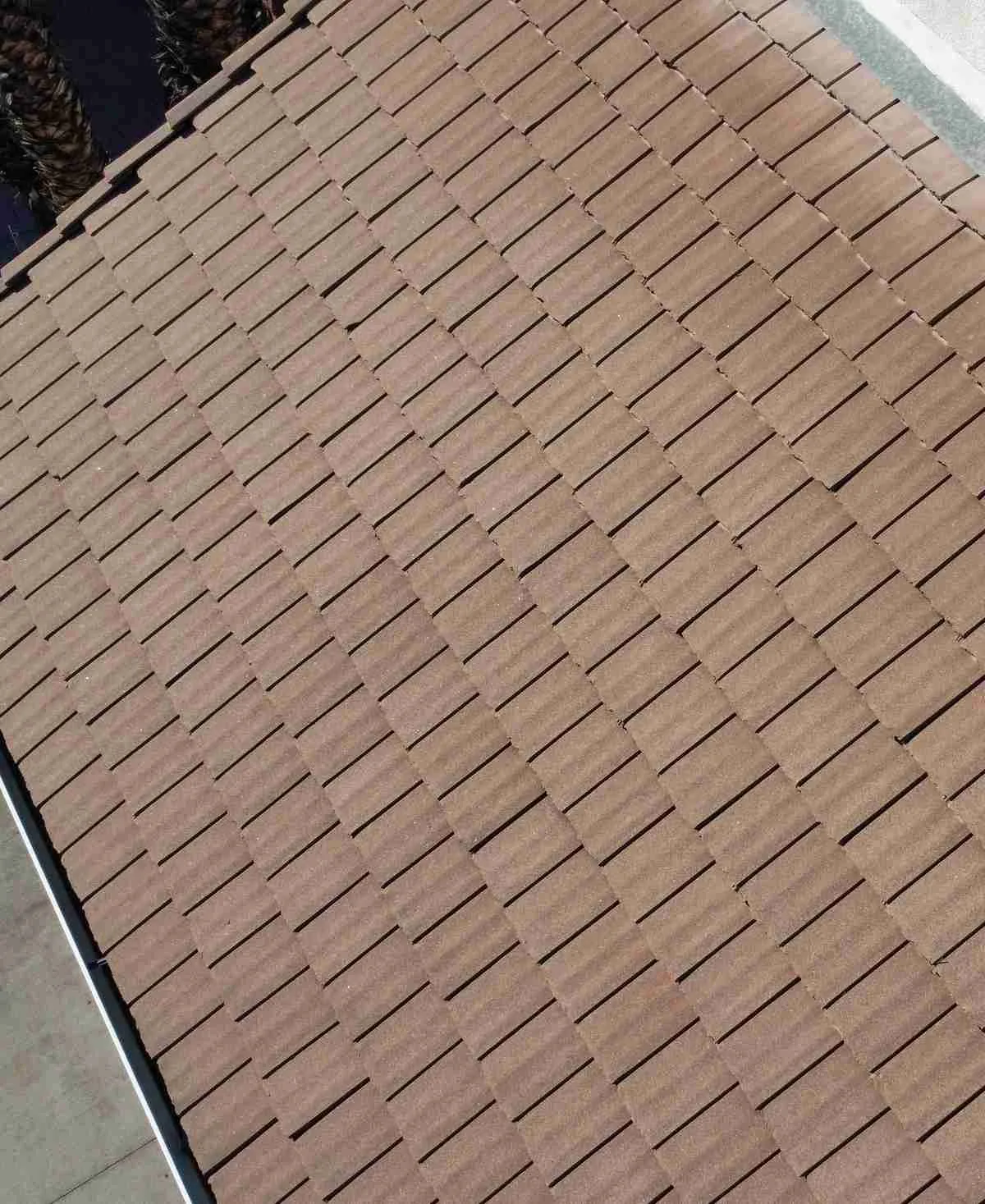 Overhead view of a brown interlocking flat tile roof beside a white stucco wall