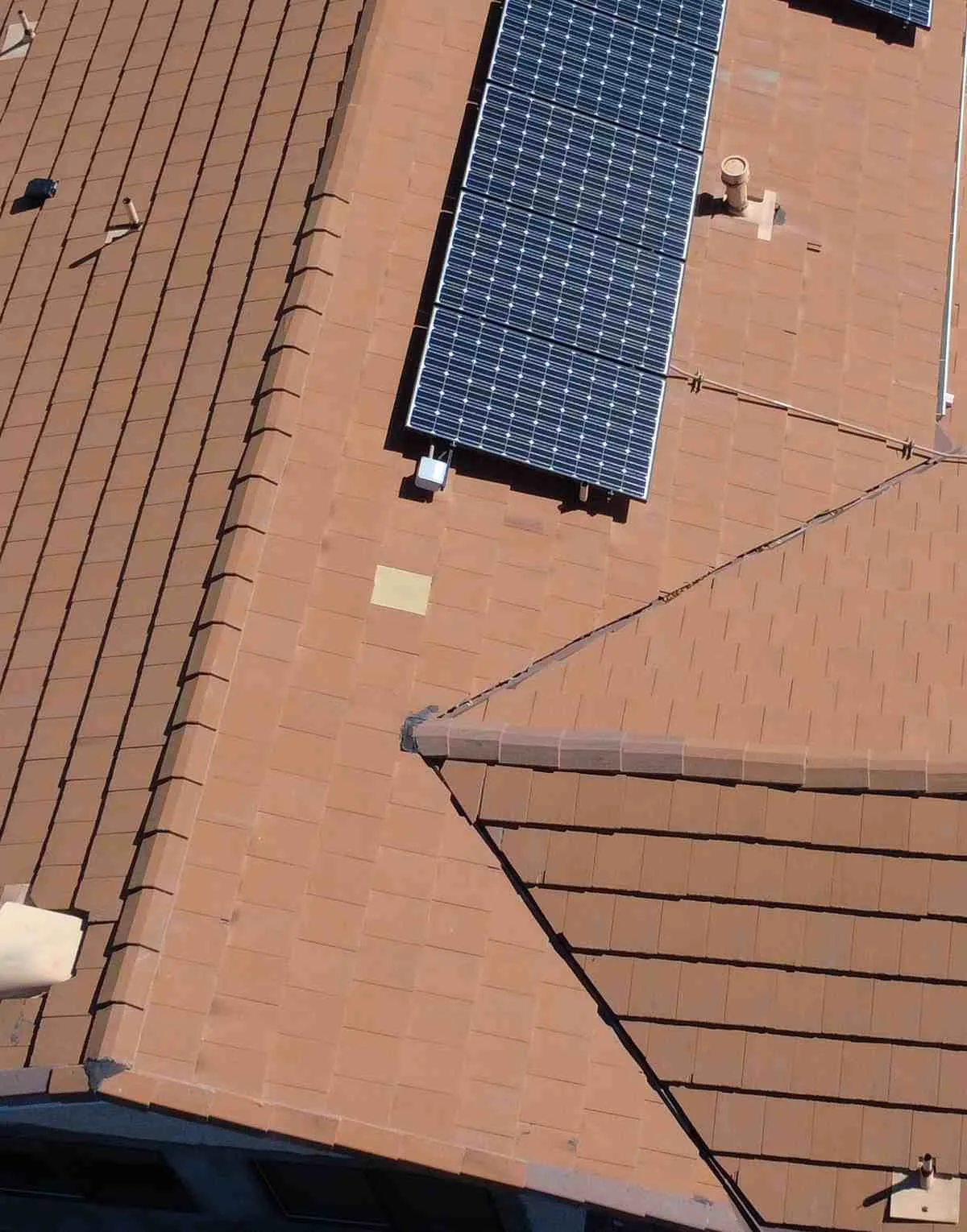 Overhead view of a brown flat tile roof with dark solar panels, conduit and a vent