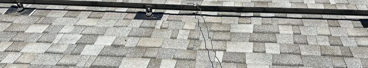Close view of gray architectural shingles with a horizontal mounting rail, rail bases and loose black cable