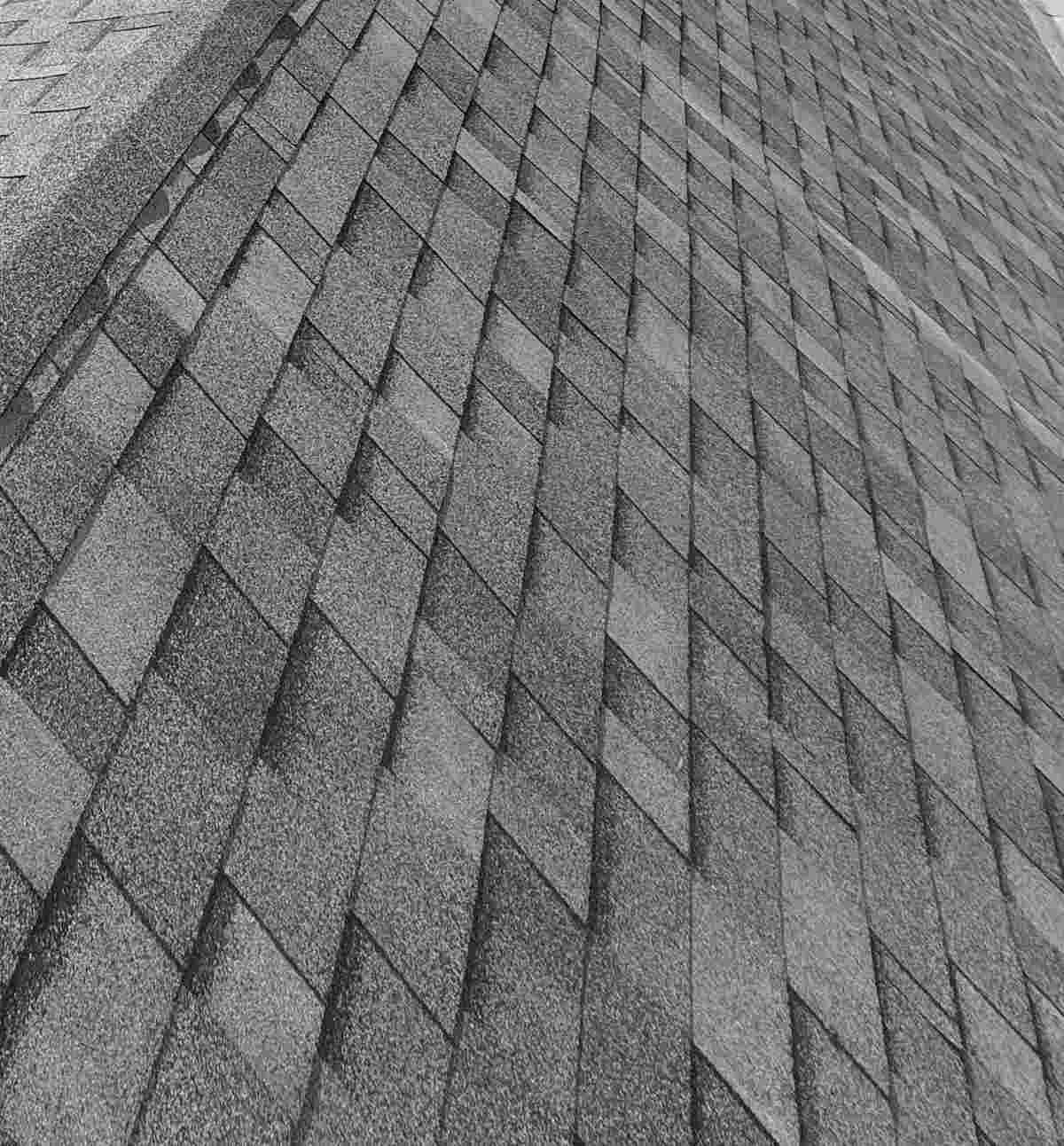 Gray asphalt shingle roof plane and ridge seen from above under a bright sky.