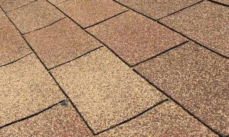 Close view of brown asphalt shingles on a sloped roof with the eave edge along the top