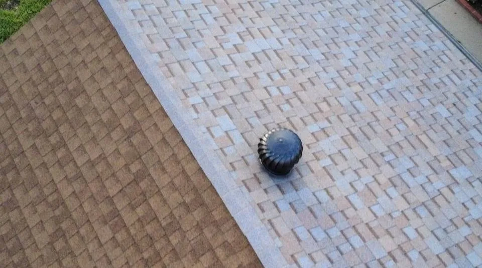Two adjoining asphalt shingle roof planes, one tan and one light gray, with a black roof vent at the sloped transition