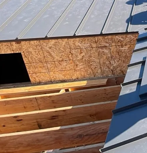 Dark gray standing seam metal roof panels beside OSB roof deck framing with rectangular roof openings