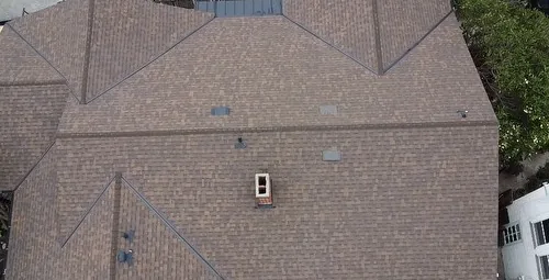 Aerial view of a broad brown asphalt shingle roof with several hips, ridges and small roof penetrations