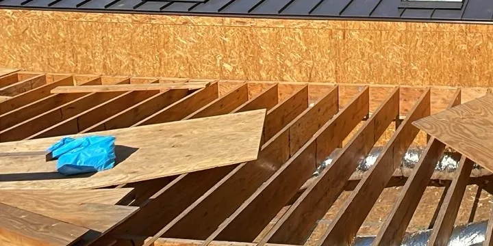 Dark standing-seam metal panels above open wood roof deck framing with rectangular openings