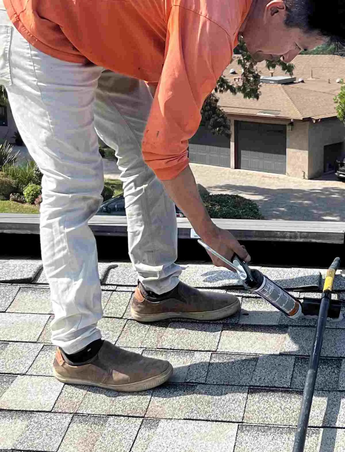 Worker applying sealant where a rail is mounted on a gray shingle roof